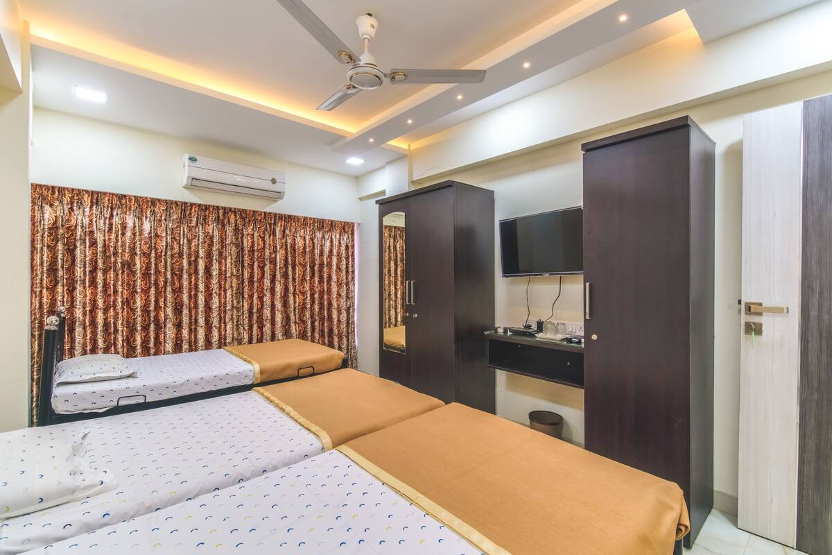 A hotel room with a bed, a wardrobe, a television, and an air conditioning unit.