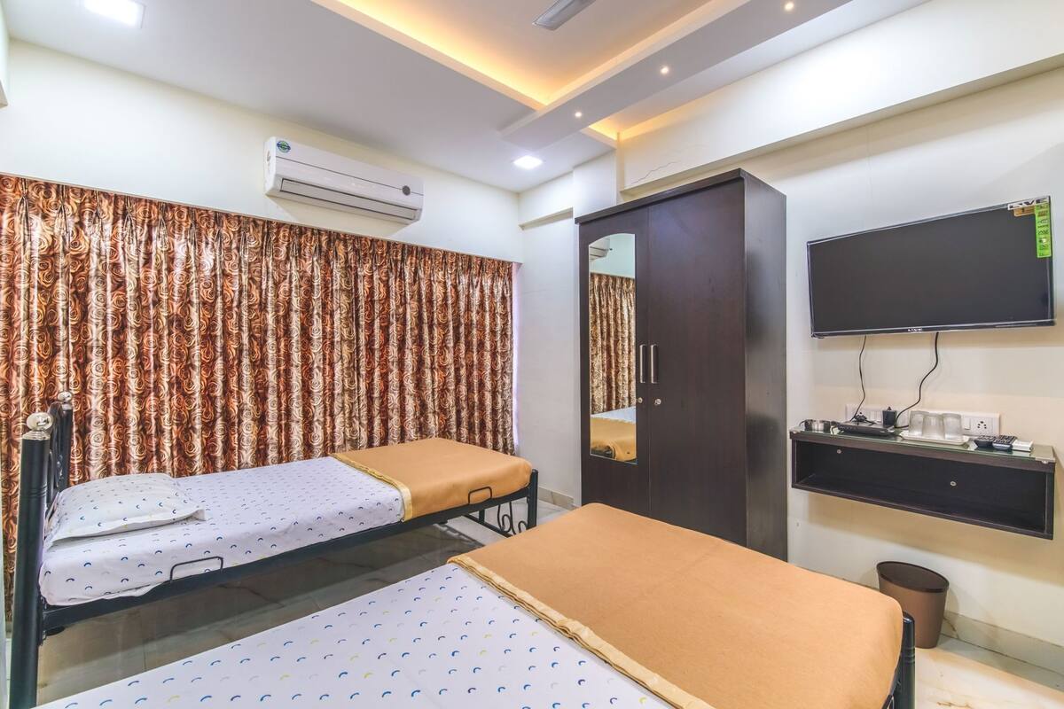 A hotel room with two beds, an air conditioner, a wardrobe, a TV, and a bedside table with a lamp.