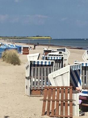 Strandhytter med randiga markiser, en sandstrand och havet i bakgrunden.