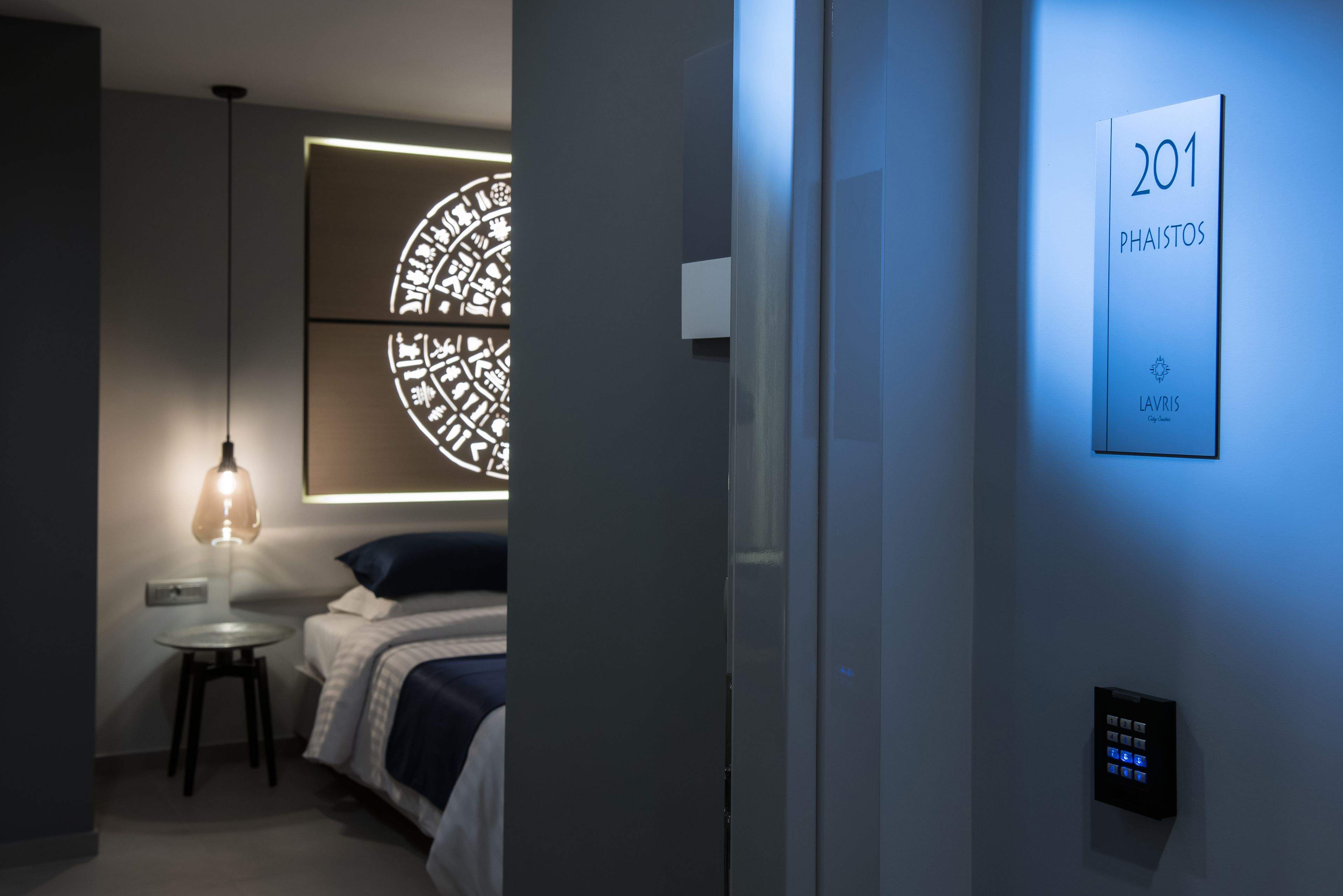 A modern hotel room with a bed, a wall-mounted light, a decorative wall piece, and a digital keypad.