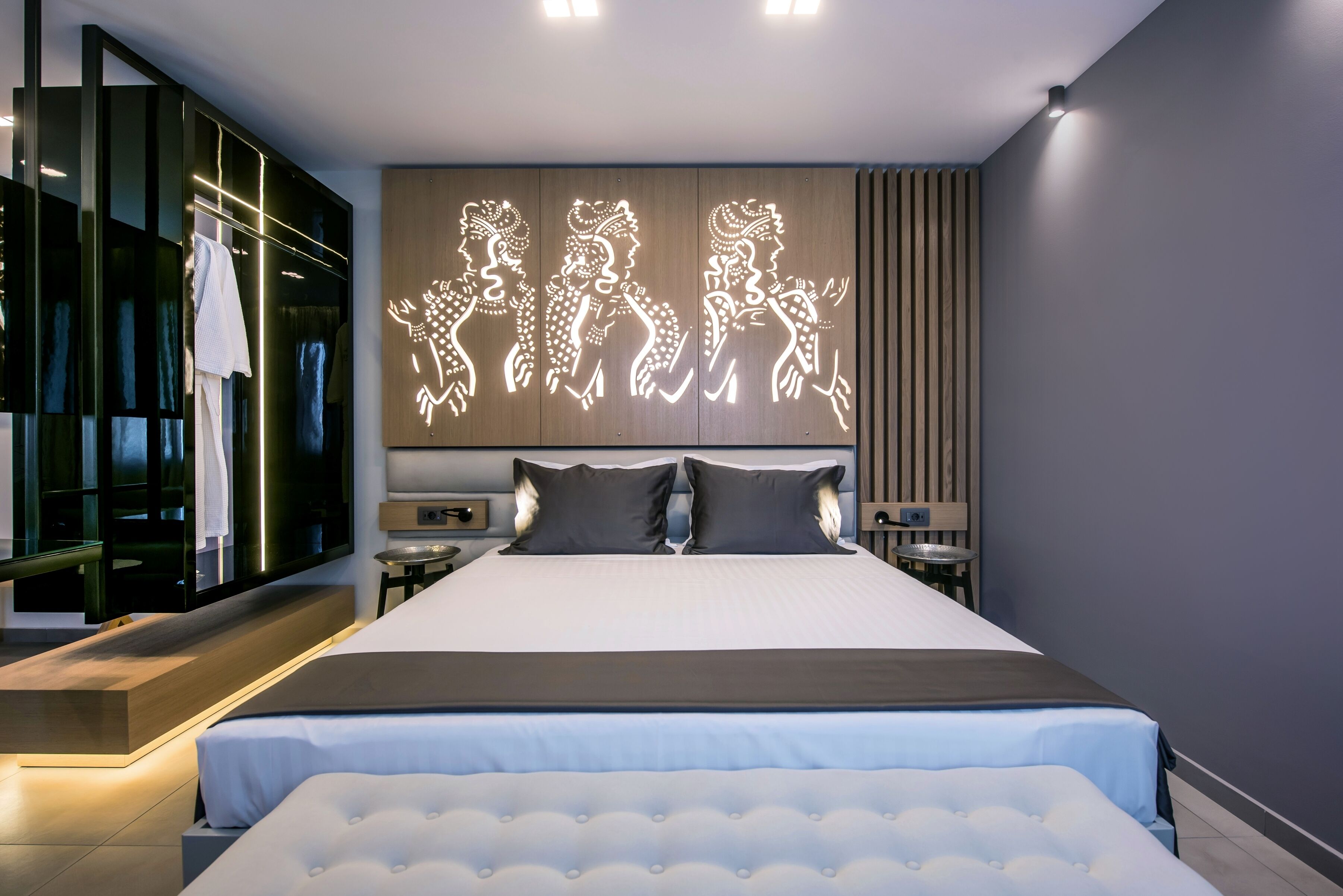 Una habitación de hotel moderna con una cama grande, un televisor montado en la pared y una obra de arte iluminada y original sobre la cama.