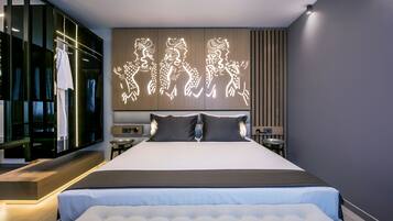 Una habitación de hotel moderna con una cama grande, un televisor montado en la pared y una obra de arte iluminada y original sobre la cama.