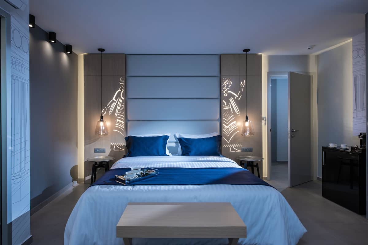 Ein modernes Hotelzimmer mit einem großen Bett, zwei Nachttischen, einem kleinen Schreibtisch und einer Wandleuchte.