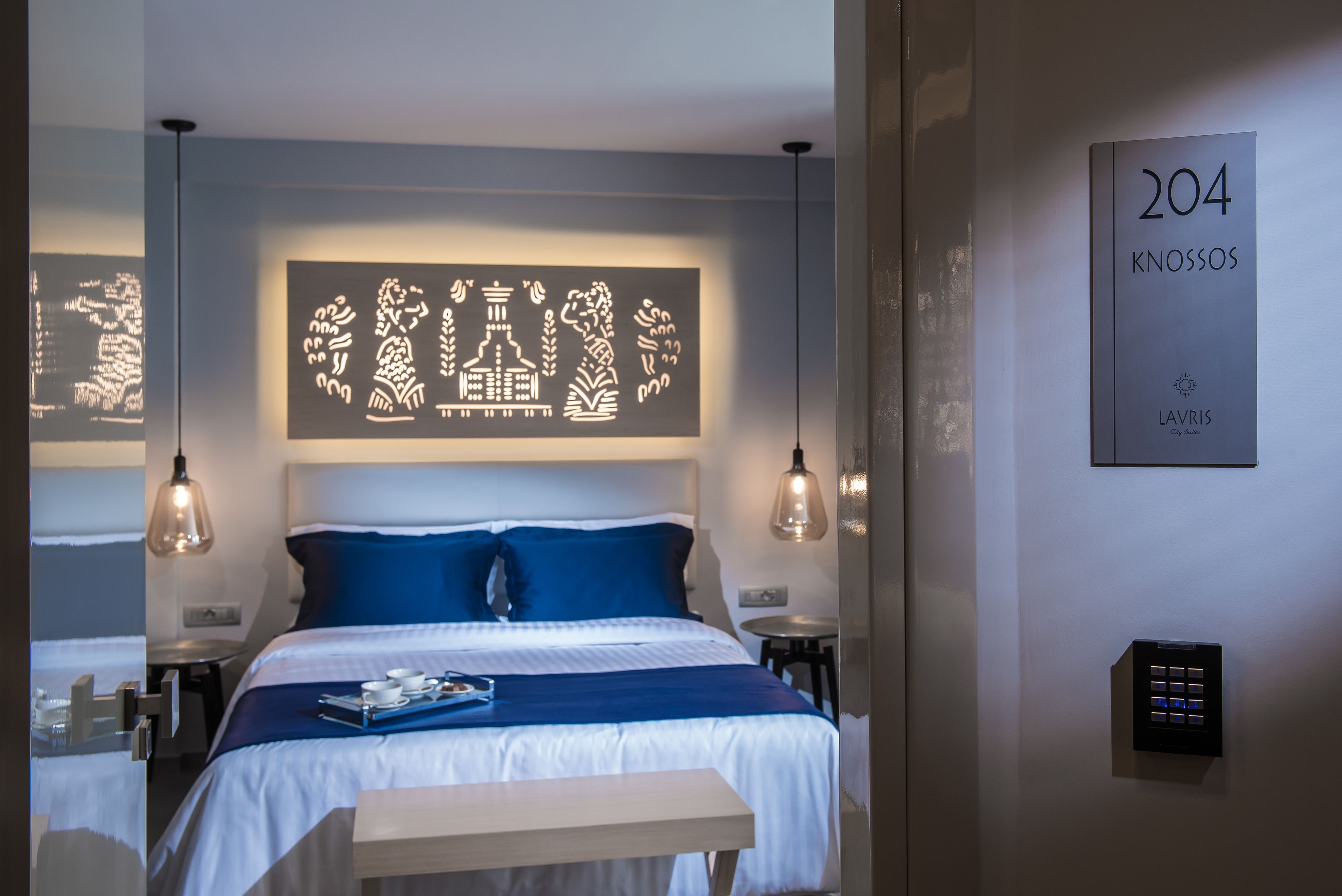 Ett hotellrum med en säng, sängbord, ett litet bord, en väggmonterad lampa och en skylt med rumsnumret.