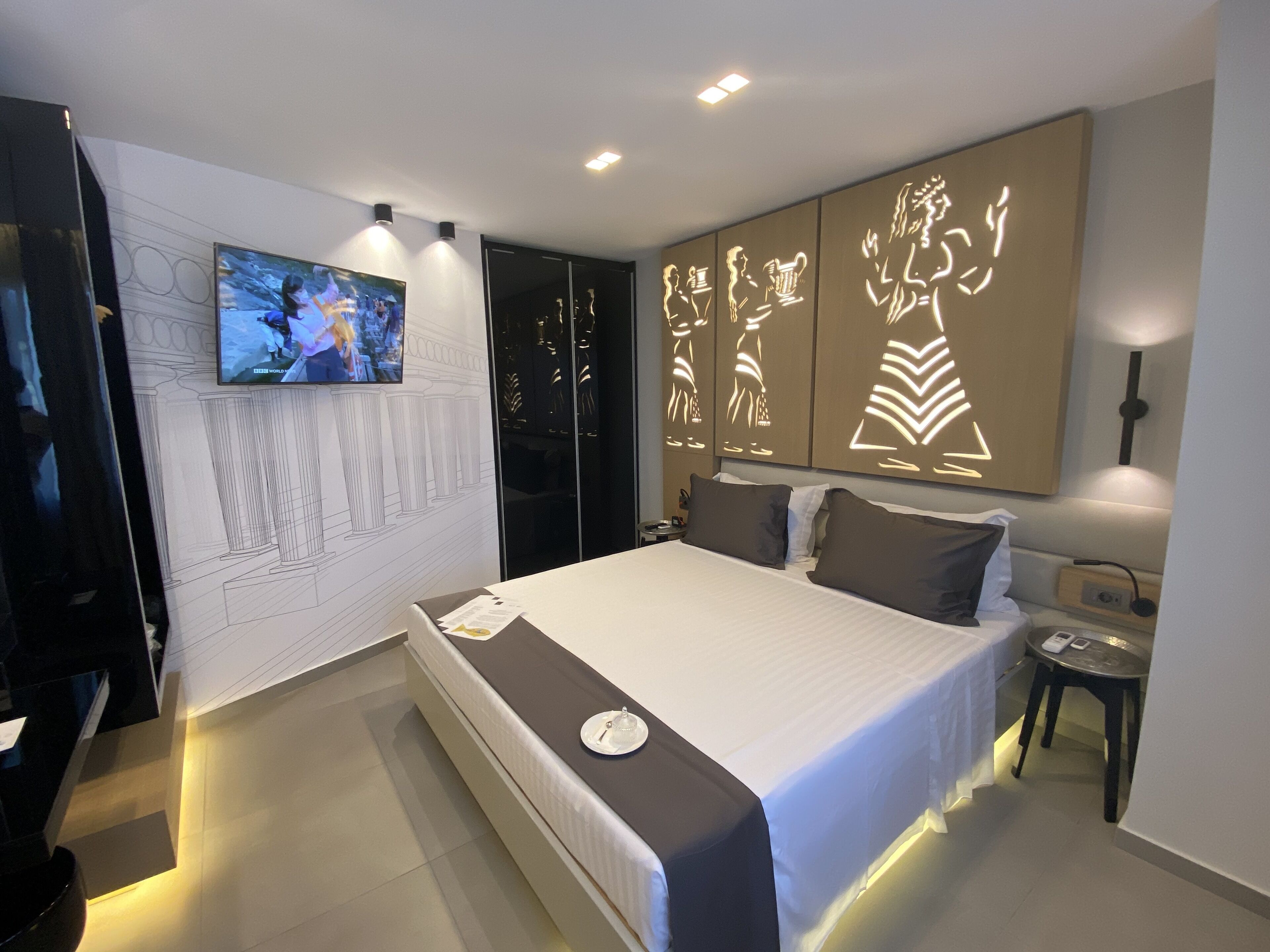 Une chambre d’hôtel moderne dotée d’un grand lit, d’un téléviseur à écran plat fixé au mur et d’un panneau décoratif mural.