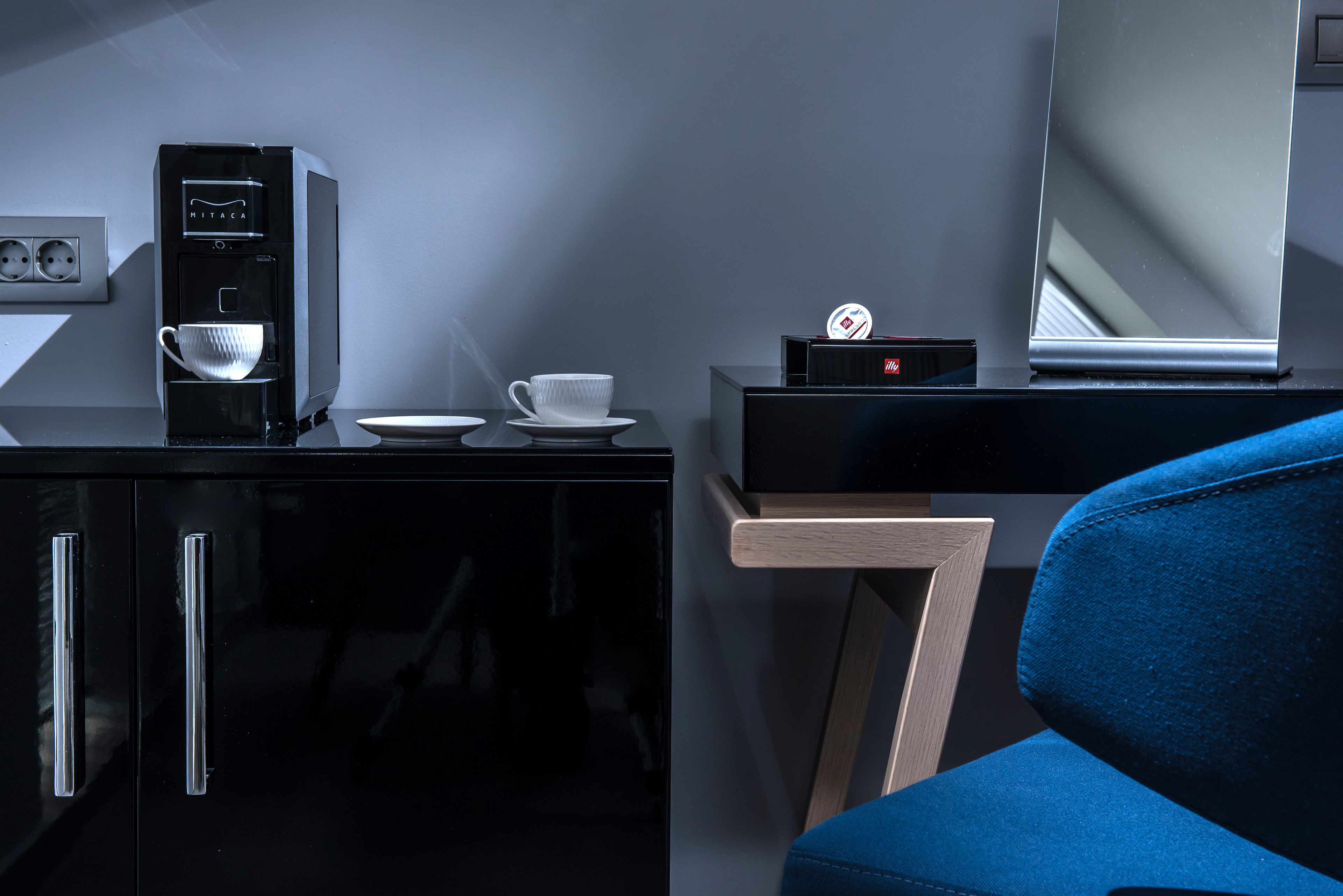 A modern room with a black cabinet, a coffee machine, a cup, a small table, and a blue chair.