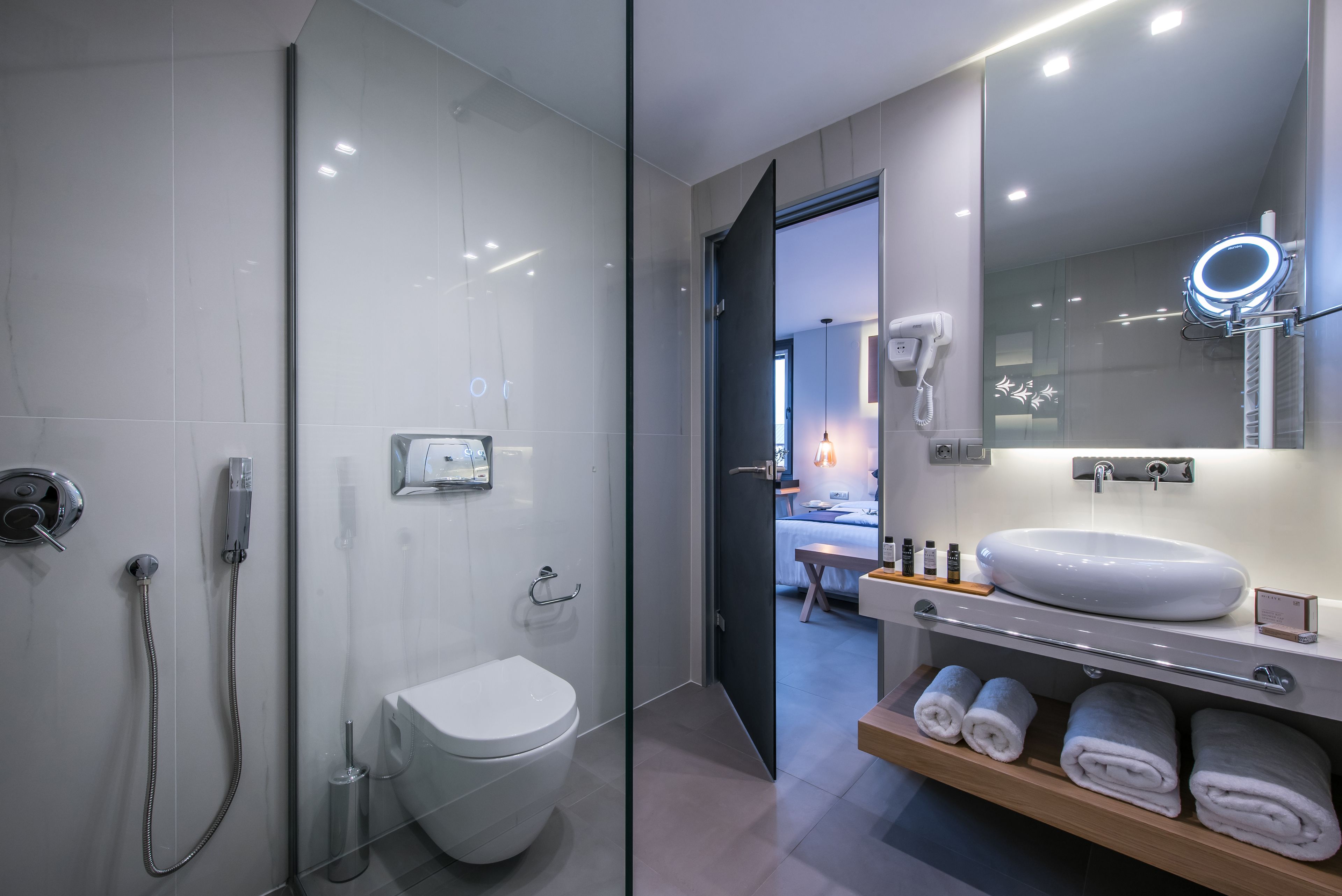 A modern bathroom with a glass shower enclosure, a white toilet, a vanity with a large mirror, and neatly folded towels.