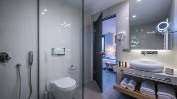 A modern bathroom with a glass shower enclosure, a white toilet, a vanity with a large mirror, and neatly folded towels.