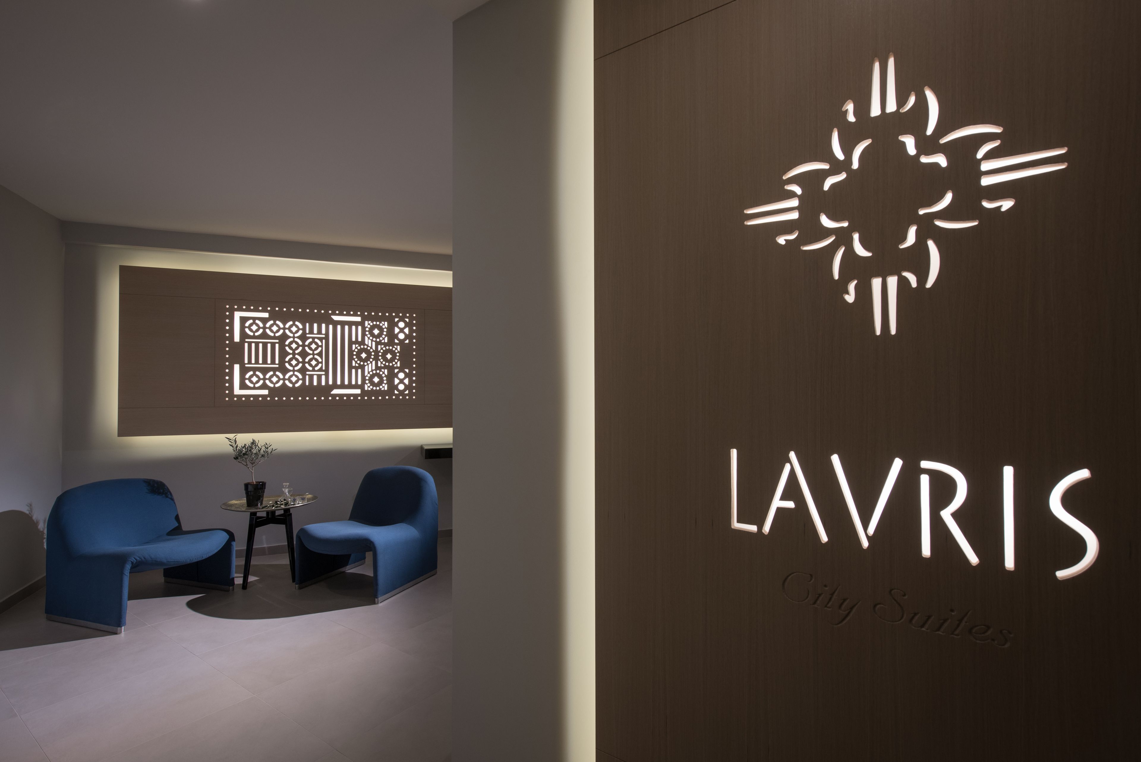 A modern interior with a city-themed wall art, a logo for 'LAVRIS City Suites', and two blue chairs in a seating area.