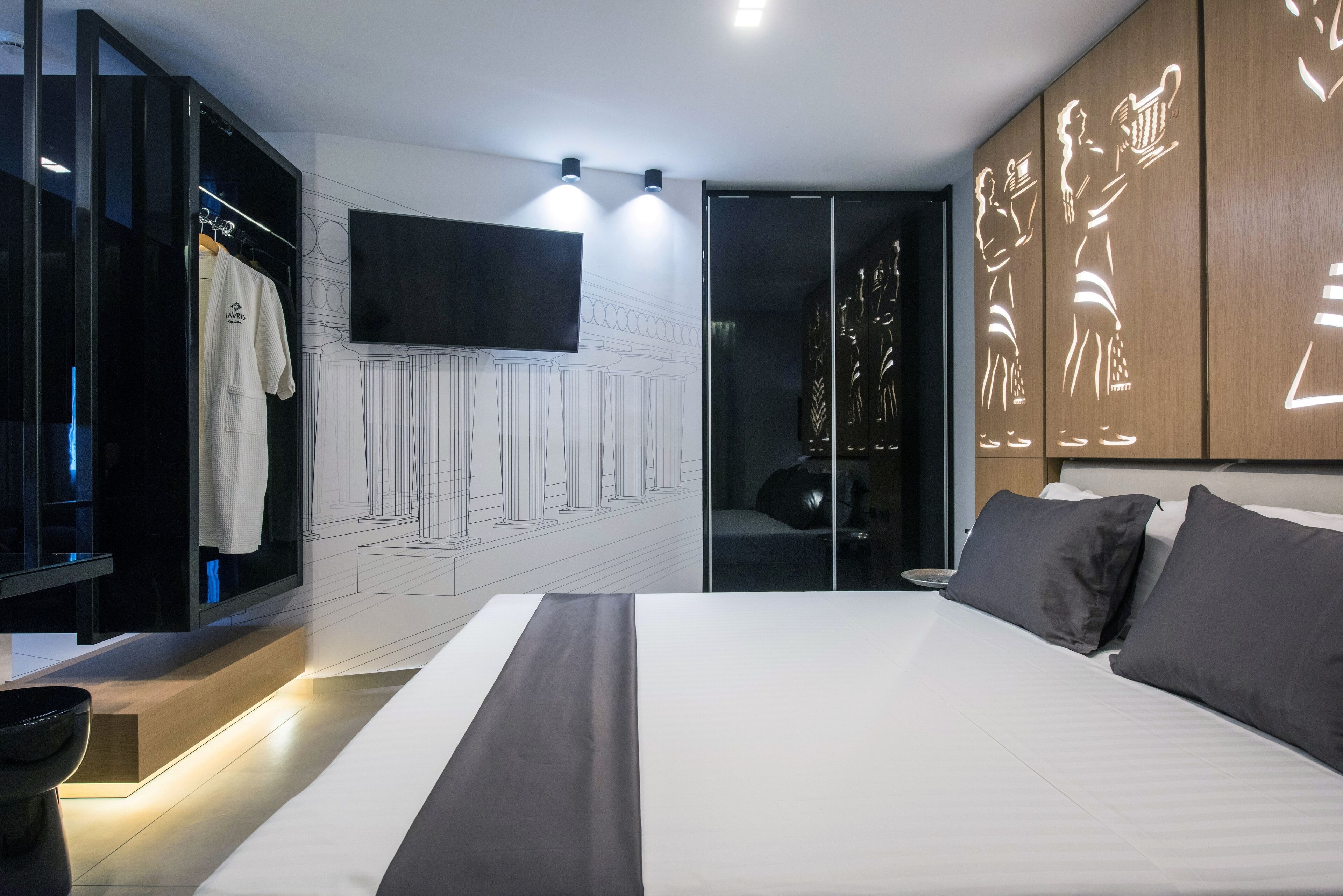 A modern bedroom with a large bed, a wardrobe with a mirror, a flat-screen TV, and a wall with decorative lighting.