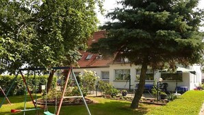 A residential area with a swing set, a well-maintained lawn, and a house with a red-tiled roof. - Room 1 - Rügen apartment 52 (Schaprode auf Rügen)