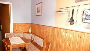 A corner dining area with a wooden table and cushioned chairs, a wooden partition wall, and kitchen utensils hanging on the wall. - Room 1 - Rügen apartment 52 (Schaprode auf Rügen)