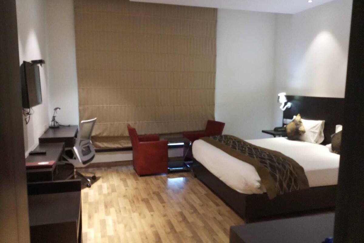 A hotel room with a bed, a desk, a chair, a TV, and a window with curtains.