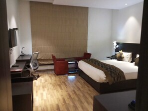A hotel room with a bed, a desk, a chair, a TV, and a window with curtains. - Joy Inn & Suites (Tijara)