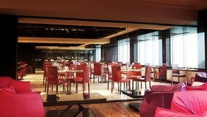 Un espace de restauration moderne avec des chaises et des tables rouges, de grandes fenêtres et un plafond haut.