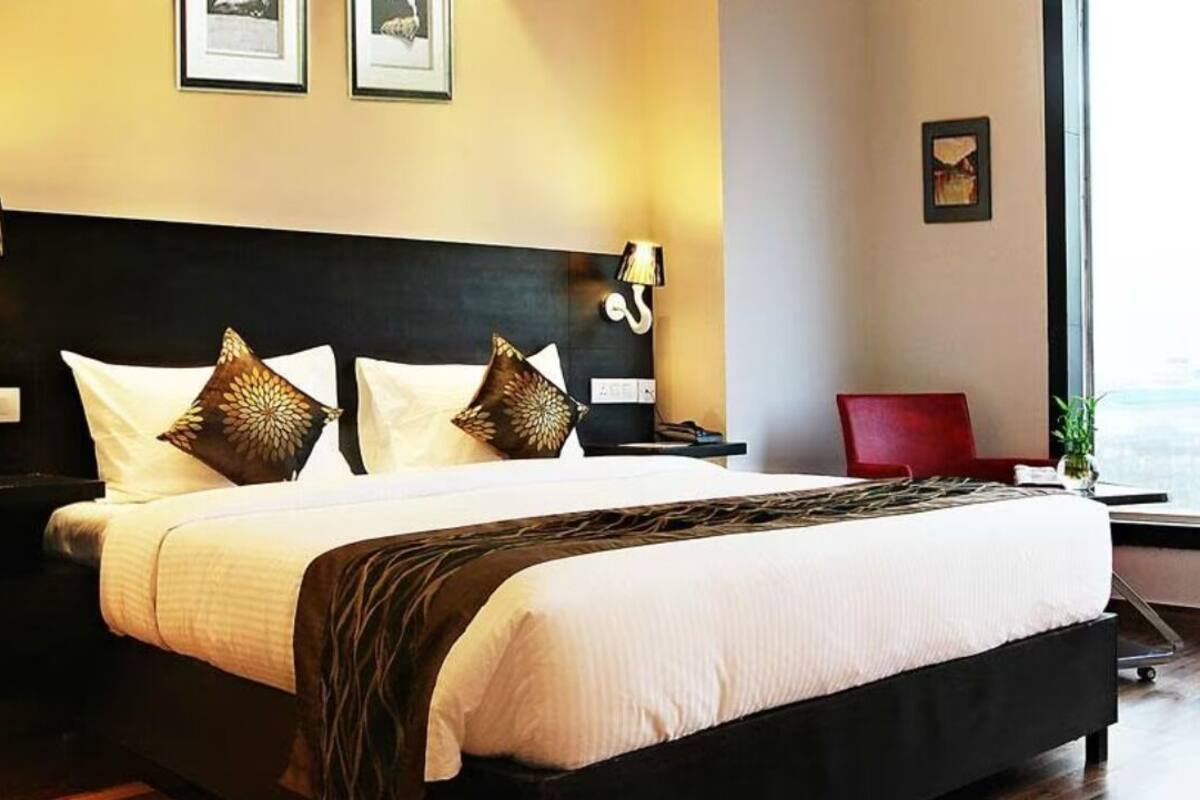 A hotel room with a large bed, a nightstand, a red chair, and a window with a view.