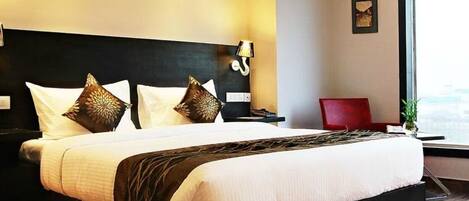 A hotel room with a large bed, a nightstand, a red chair, and a window with a view.