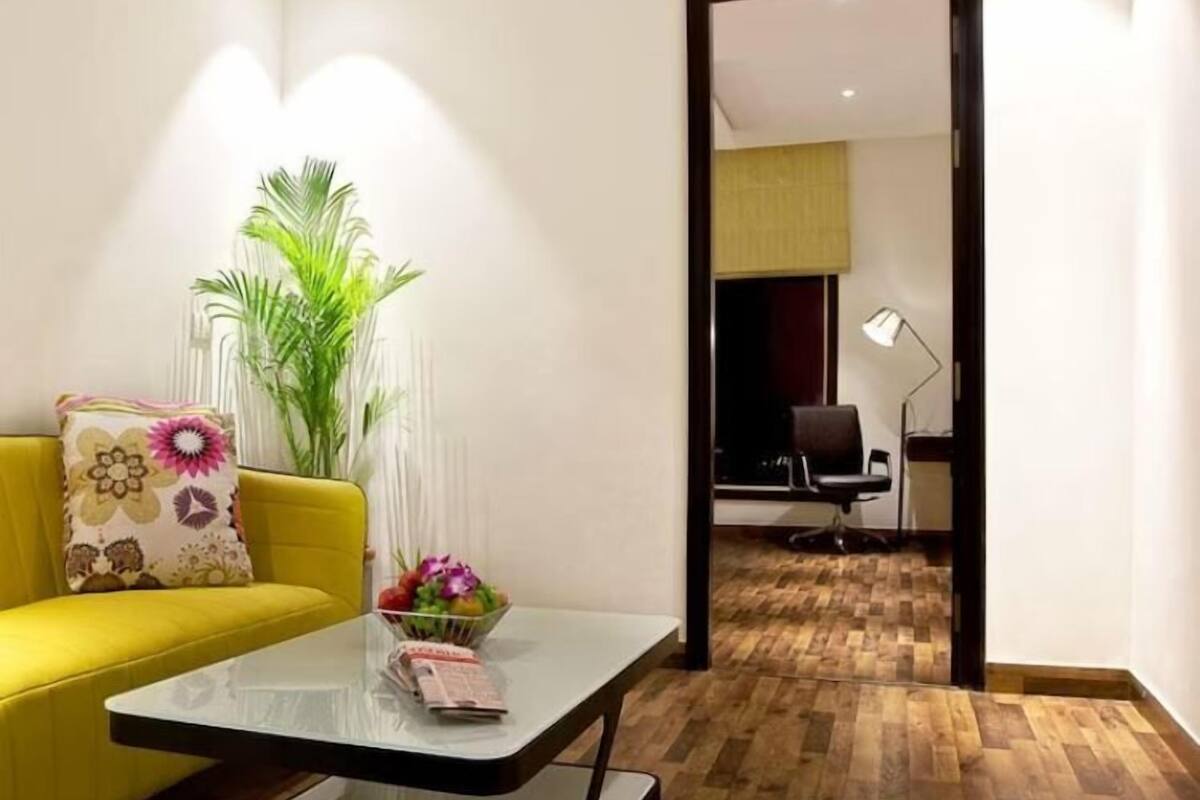 A modern living room with a yellow sofa, a glass coffee table, and a potted plant.