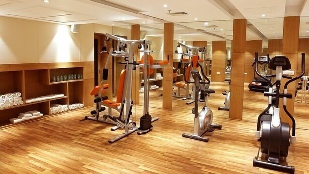 Une salle de sport équipée de divers appareils d’exercice, dotée d’un plancher en bois et de murs recouverts de miroirs.