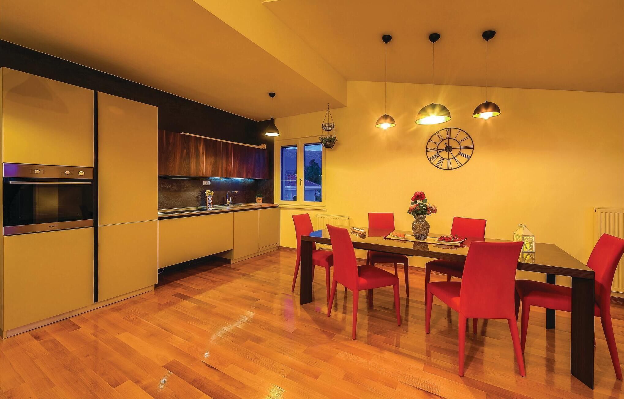 A modern kitchen with a built-in oven and a dining area with a wooden table and red chairs.