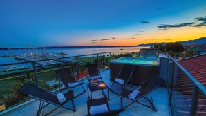 A terrace with outdoor seating and a hot tub overlooking a marina and sunset.