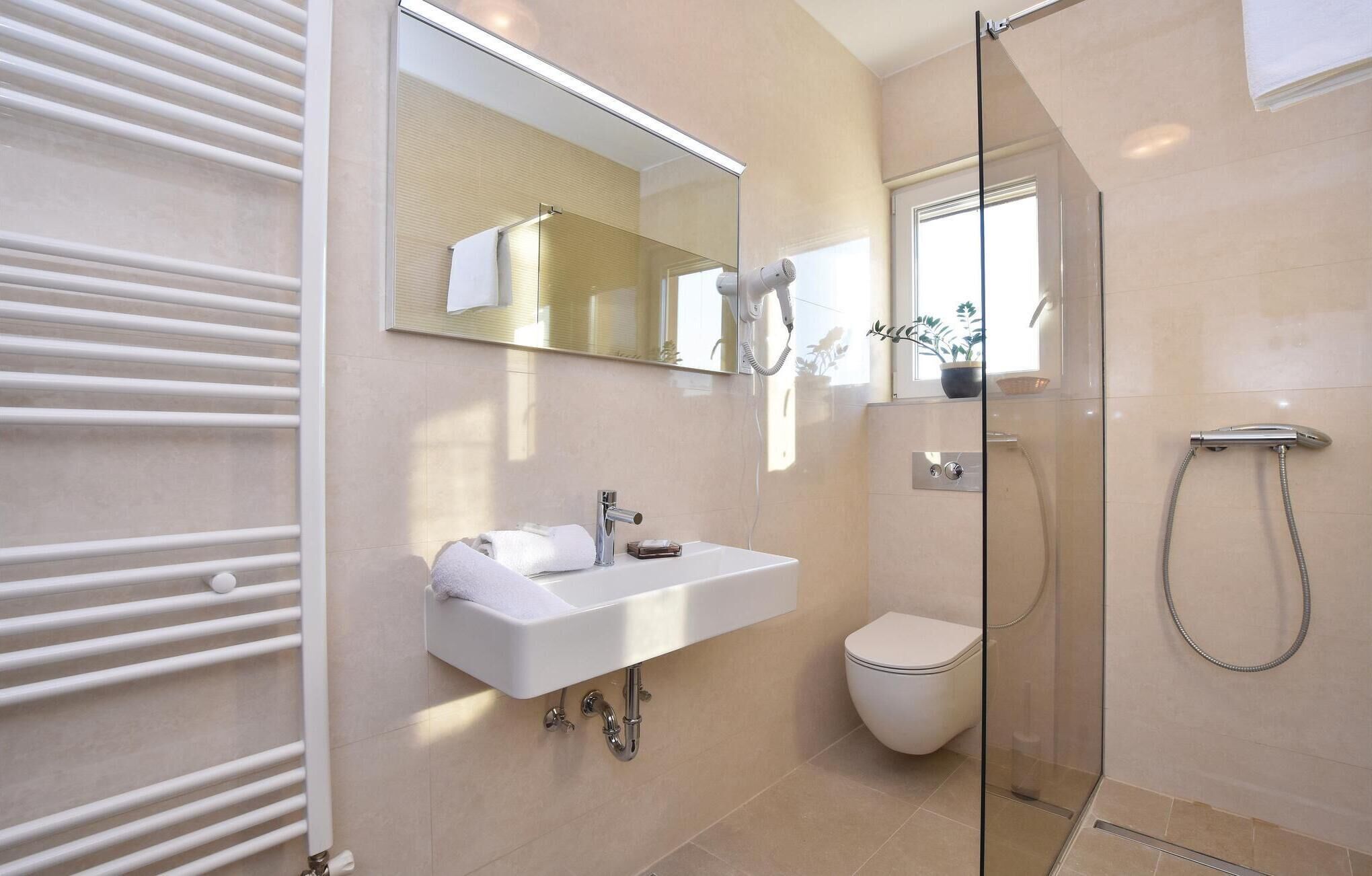 A modern bathroom with a glass shower enclosure, a white sink with a mirror above it, and a toilet.