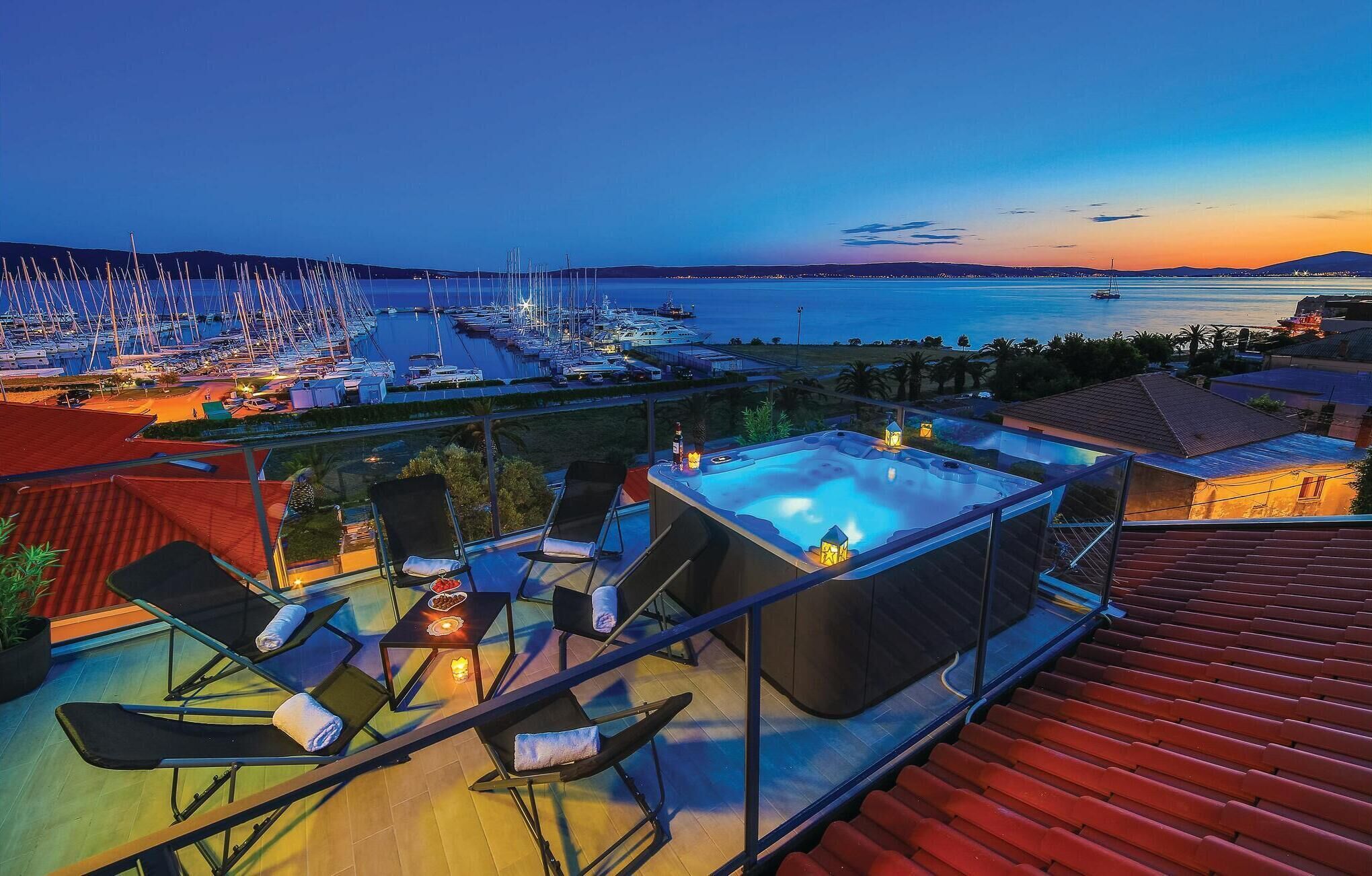 Une terrasse sur le toit avec un jacuzzi, des chaises longues et une vue sur une marina au coucher du soleil.
