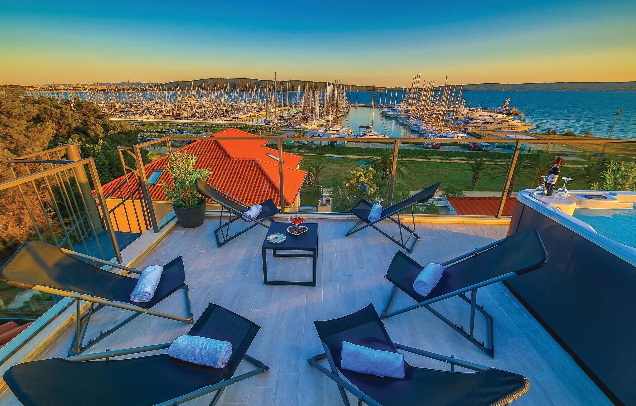 Une terrasse sur le toit, aménagée avec des chaises longues, une table et offrant une vue sur une marina remplie de bateaux.