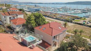 A coastal hotel with a rooftop pool, a marina with boats, and a view of the city in the background.