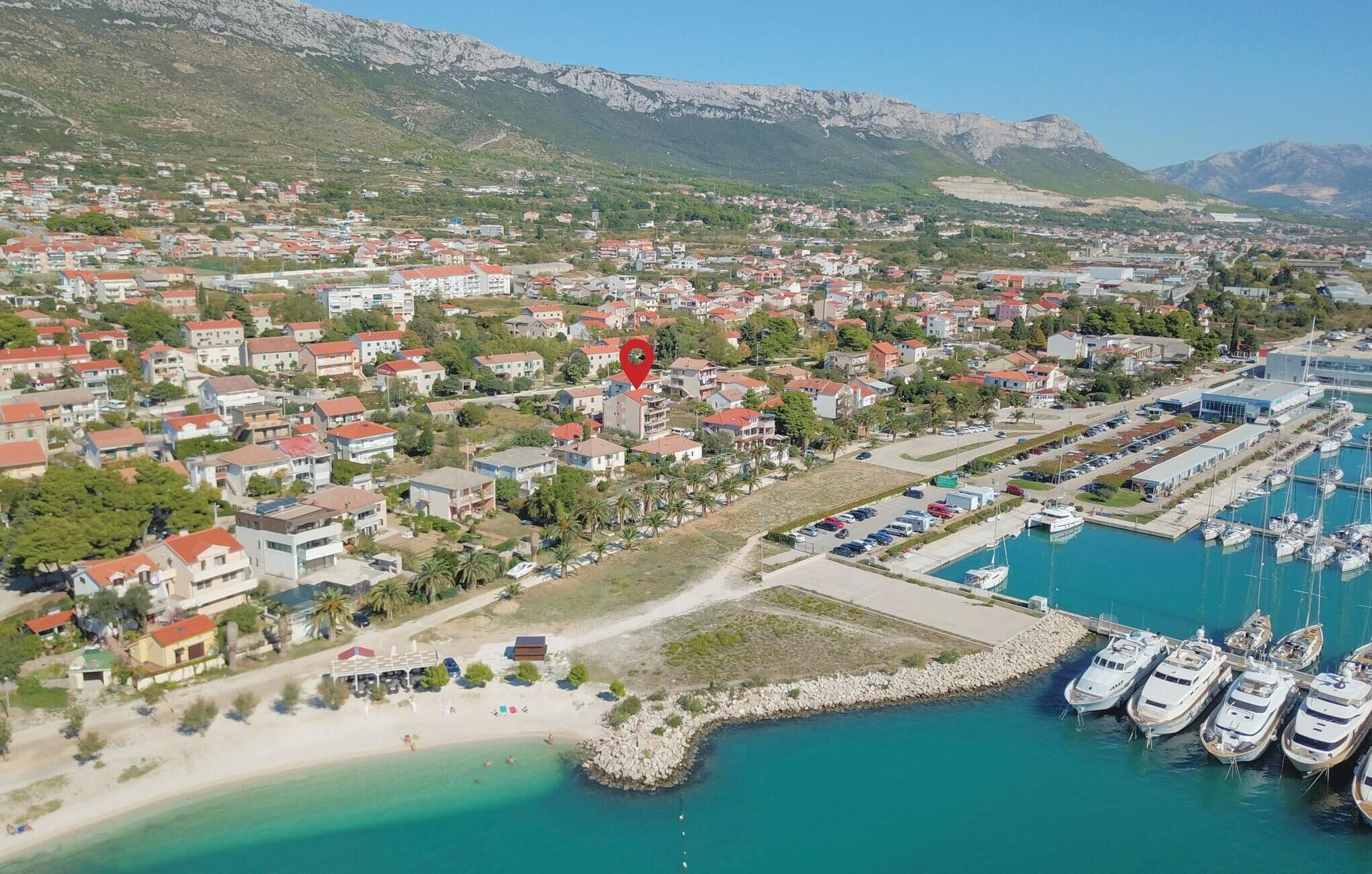 Vista aérea de un pueblo costero con edificios residenciales, un puerto deportivo con yates y una zona de playa.