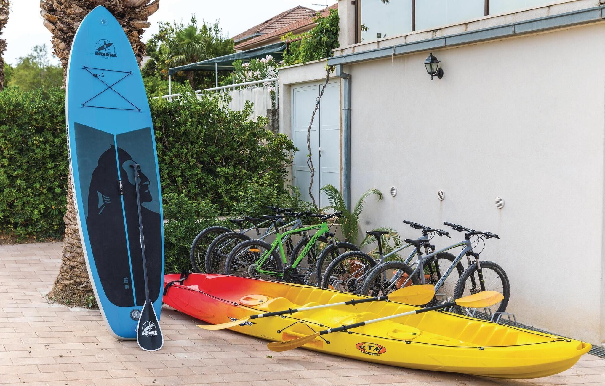 A surfboard, kayaks, and bicycles parked against a building.