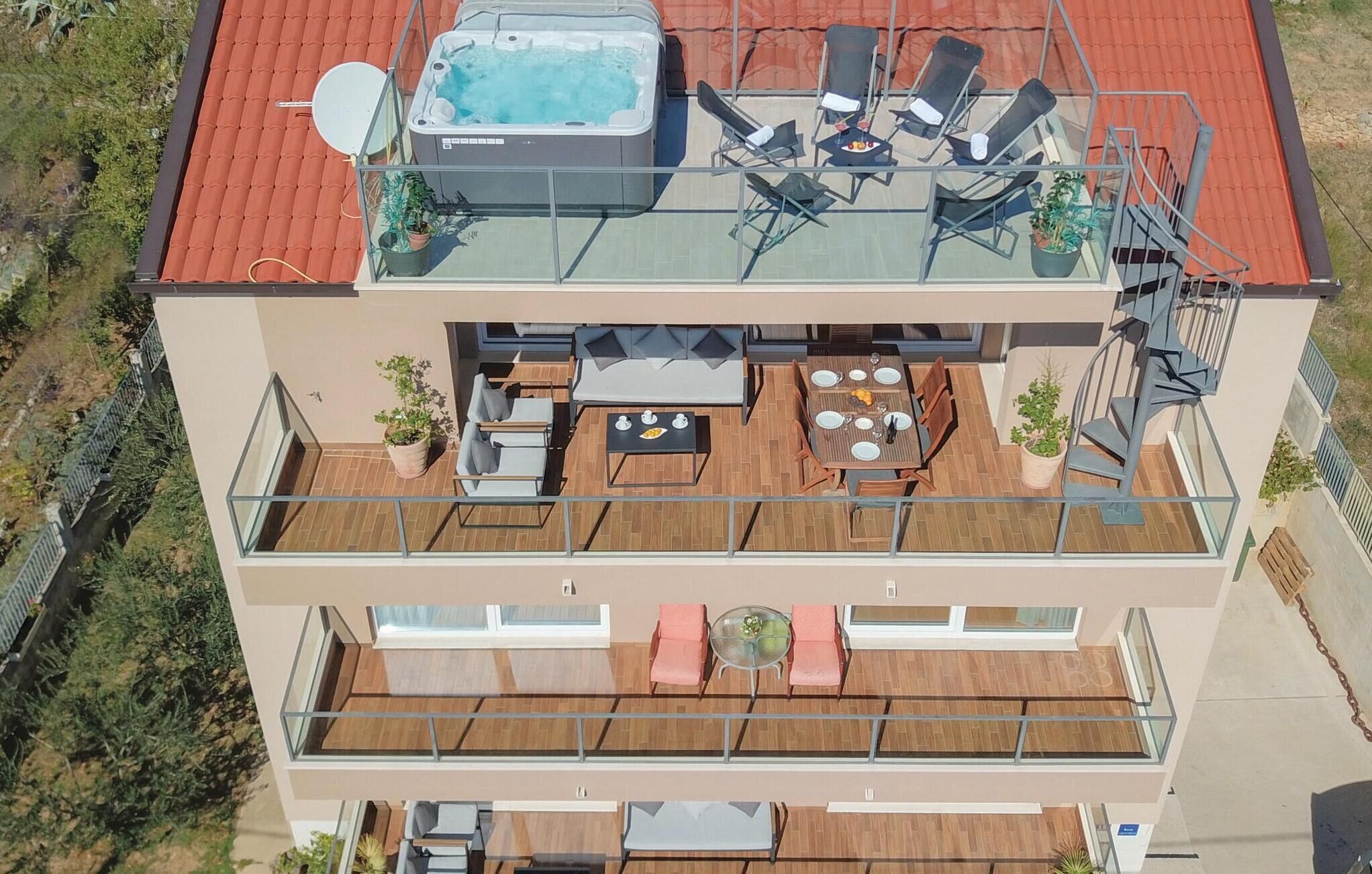 Een meerhoog gebouw met een jacuzzi op het dak, buiten zitplaatsen en een balkon met een tafel en stoelen.