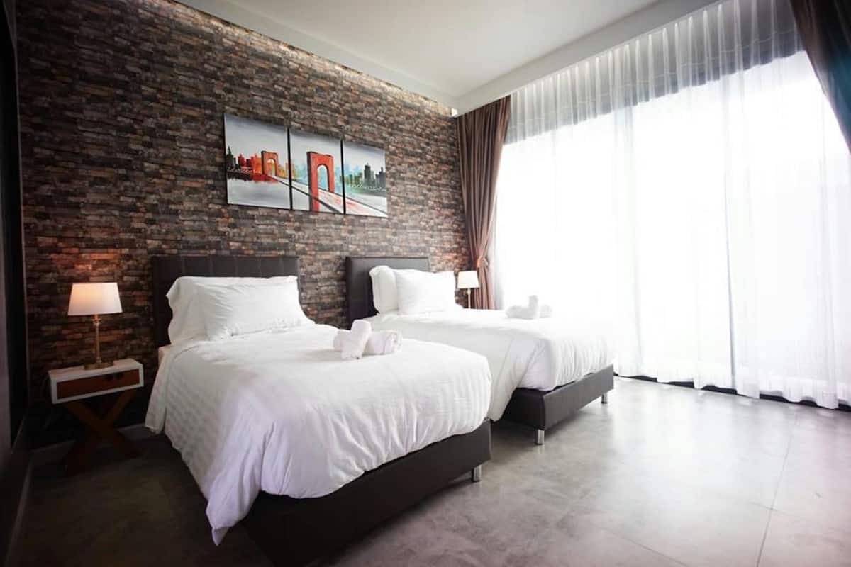 Une chambre d’hôtel avec deux lits, un mur en briques et une grande fenêtre.
