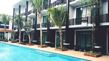 Un hotel con piscina, varios balcones y palmeras.