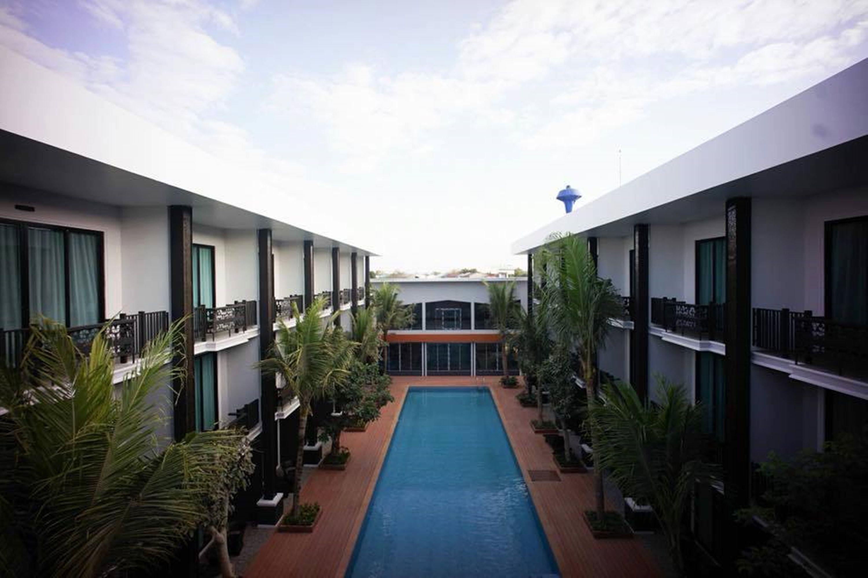Un hotel con piscina central, rodeado de múltiples pisos con balcones y vegetación.