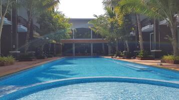 Una piscina con borde de azulejos, rodeada de palmeras y un edificio que dice "Flamingo Fit Club".