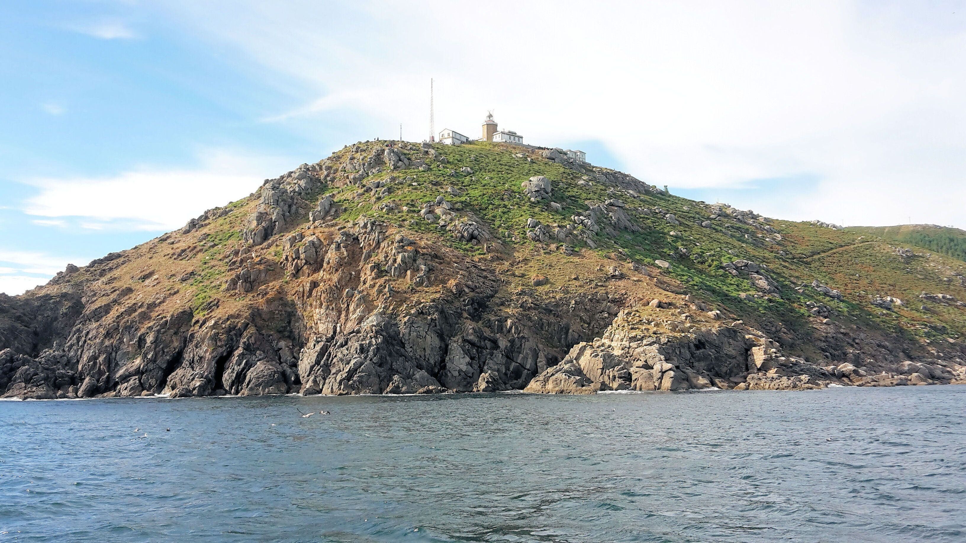 Une île rocheuse, surmontée d’un phare et d’un bâtiment, et entourée d’eau.