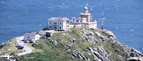 Ein Küstengebäude mit mehreren Strukturen, darunter ein Leuchtturm, auf einem felsigen Hügel mit Blick auf das Meer.