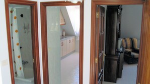 A hallway with a shower, a kitchen area, and a seating area with a chair and a table. - Lobeira do Mar (O Pindo-Carnota, LA Coruña)