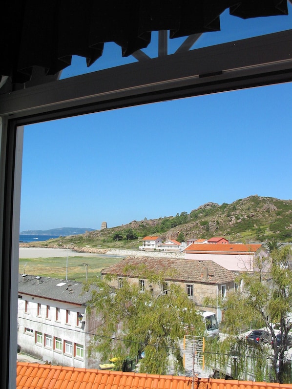 Un pueblo costero con edificios, una playa y colinas al fondo.