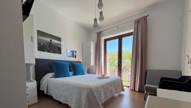 A bedroom with a bed, a desk, and a balcony with curtains. - Balcones de Bentomiz (Arenas)