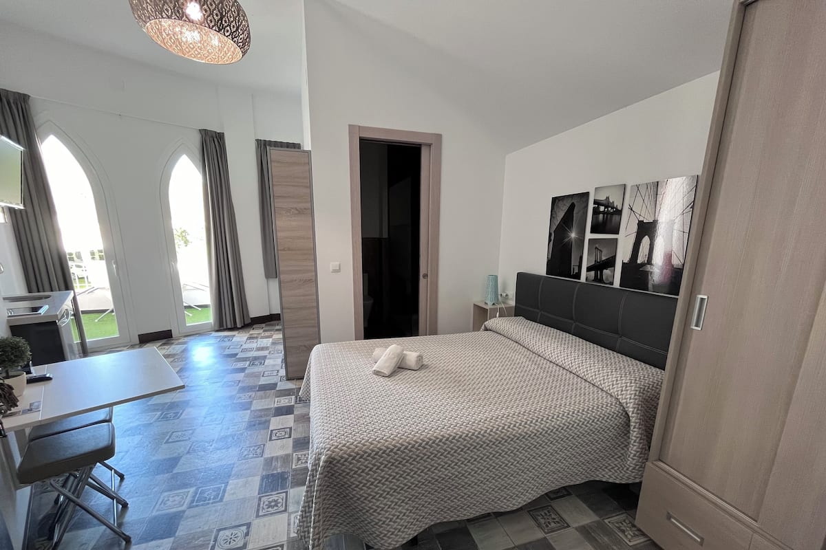 Habitación de hotel con cama, escritorio y silla. Hay una puerta que da a un balcón.