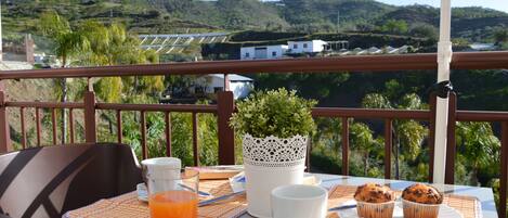 A table with breakfast items, a plant, and a scenic view of hills.