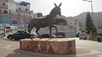 A horse statue on a pedestal in an urban setting with buildings and vehicles in the background.