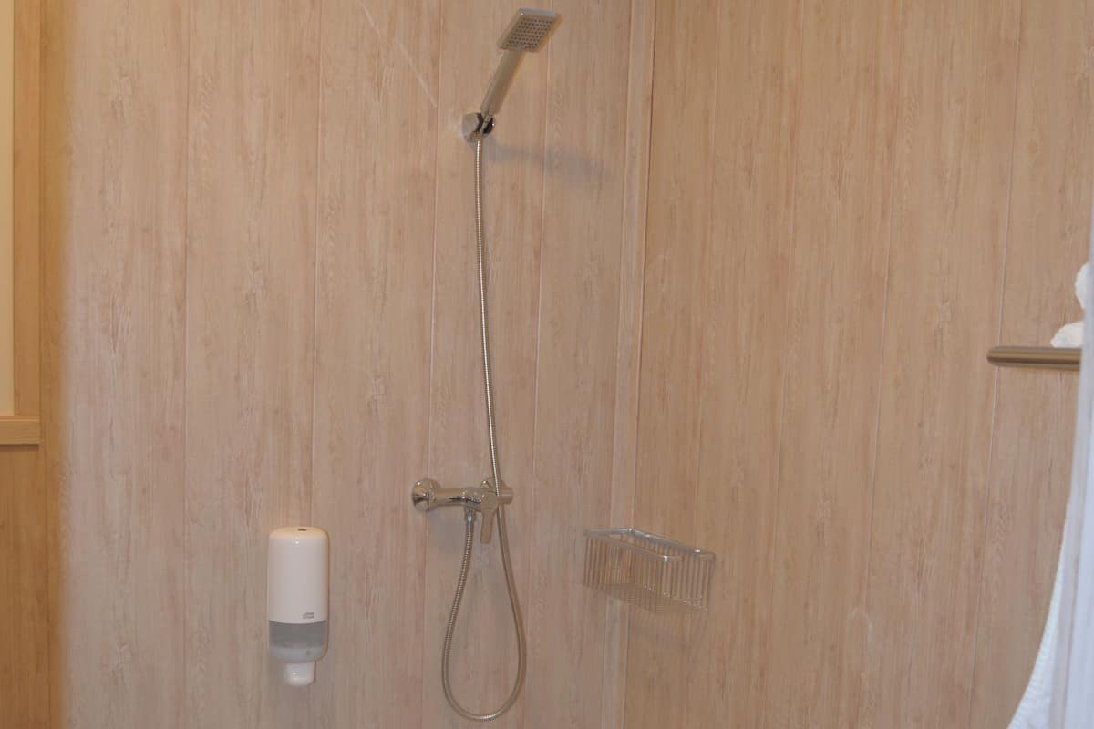 Una ducha con cabezal de ducha manual, dispensador de jabón y un estante pequeño.