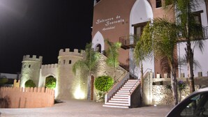 A building with a castle-like facade, named "Balcones de Bentomiz Apartahotel," featuring stone walls, arched windows, and a staircase leading to an upper level. - Balcones de Bentomiz (Arenas)