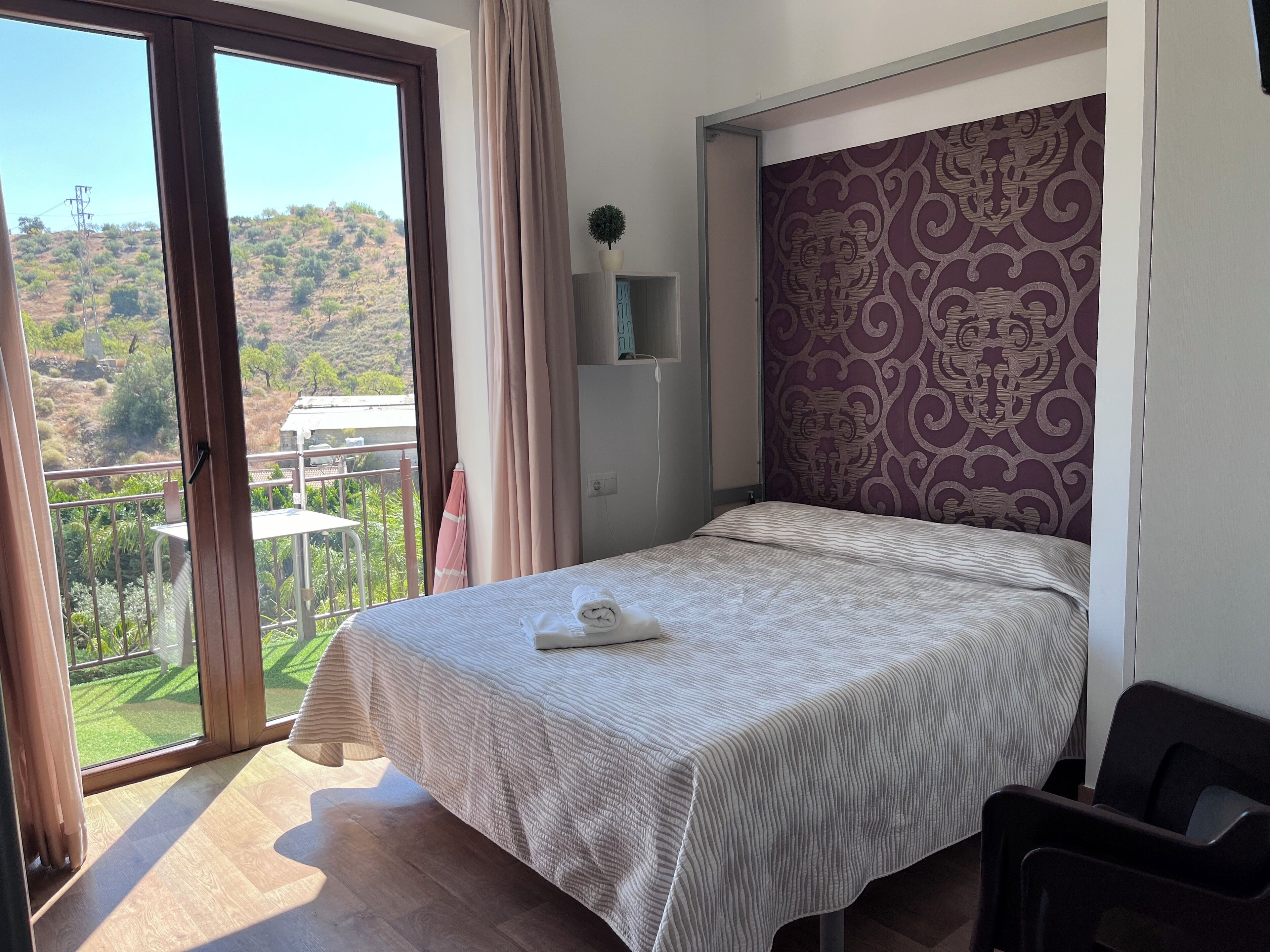 Un dormitorio con cama, vistas a un balcón y una pared decorada.