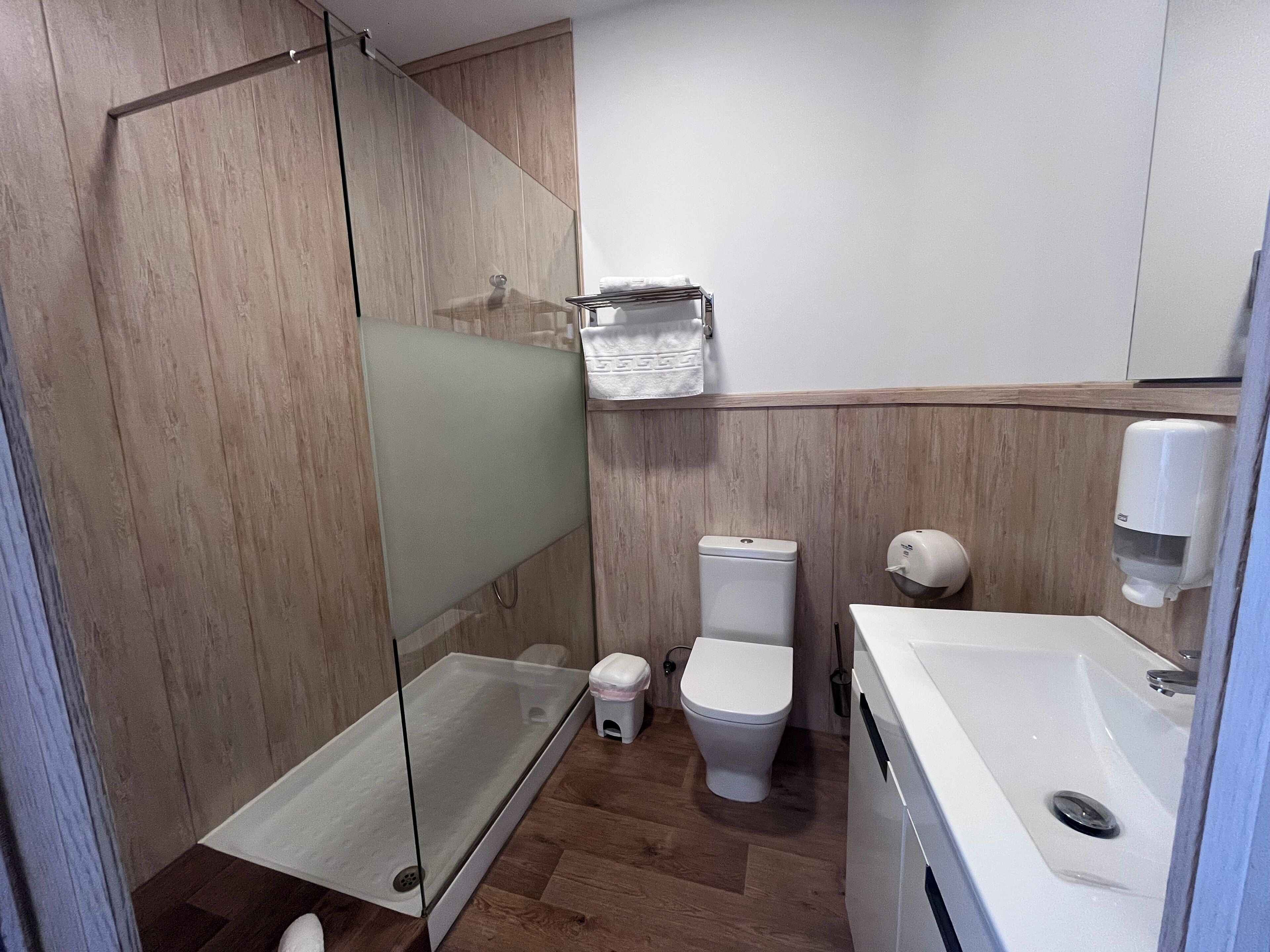 A modern bathroom with a glass shower enclosure, a toilet, and a sink with a soap dispenser.