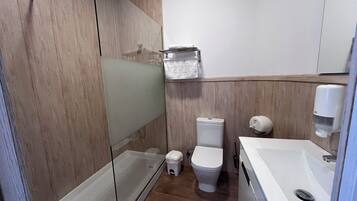 Un baño moderno con cabina de ducha de vidrio, un inodoro y un lavabo con dispensador de jabón.