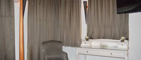 A hotel room with a bed, a chair, a desk with drawers, a television mounted on the wall, and curtains covering the windows.